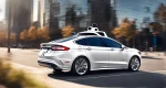 The image features a sleek, white Ford self-driving car with sensors and cameras mounted on the exterior.