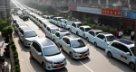 The image shows a hybrid car on a congested city street in China, with a prominent display of solar panels on the rooftop.