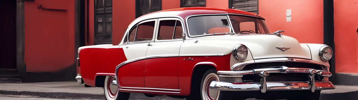The image shows a vintage classic car with a glossy red exterior, chrome bumpers, and white-wall tires.